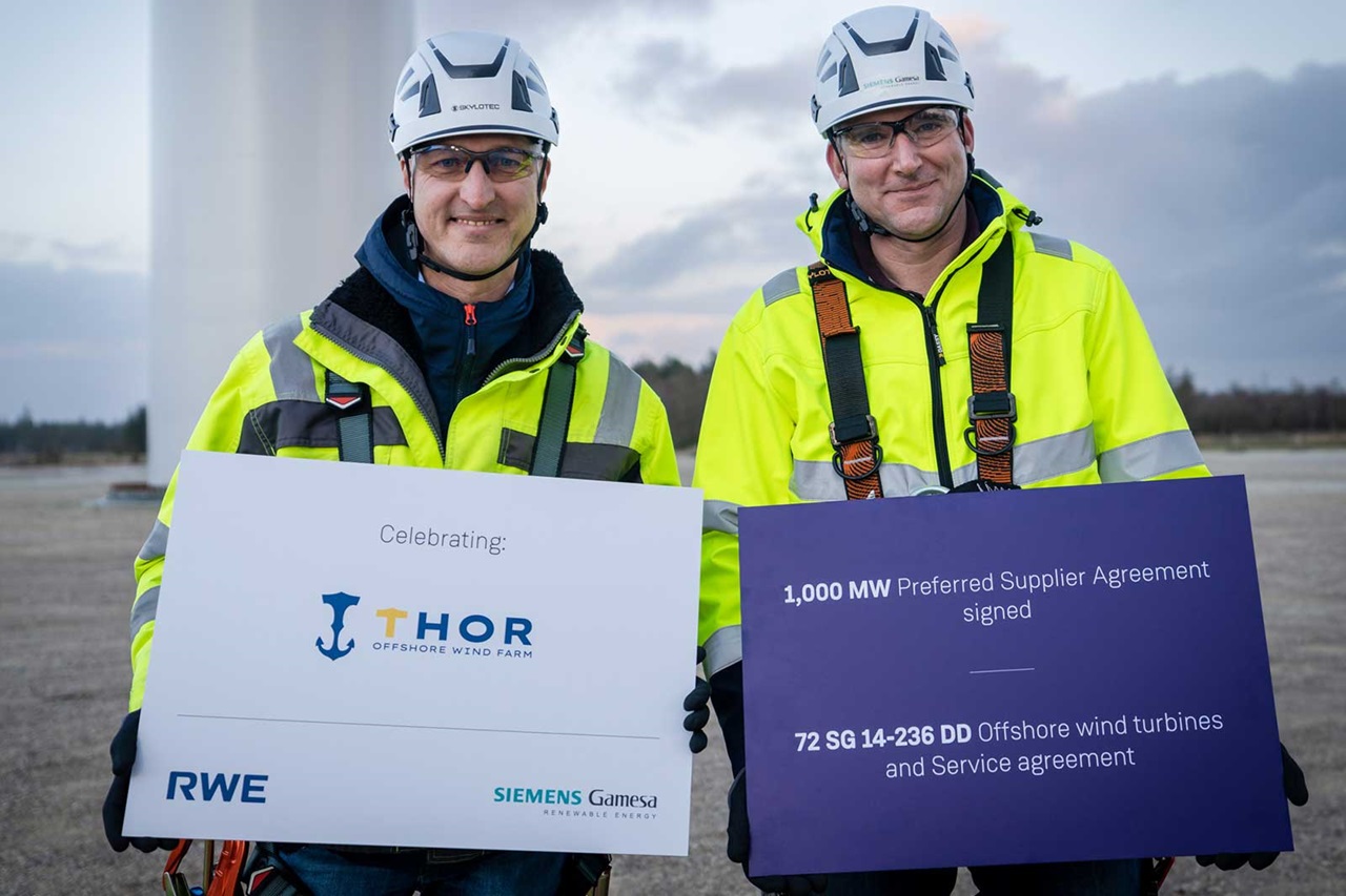 To personer i sikkerhedstøj holder skilte, der fejrer en aftale om offshore vindmølleparken THOR.