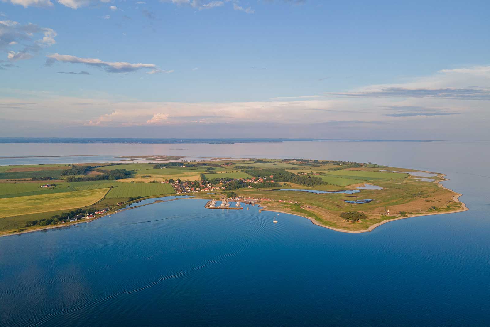 Et luftbillede af et landligt område med en kystlinje, grønne marker og en rolig bugt ved havet.