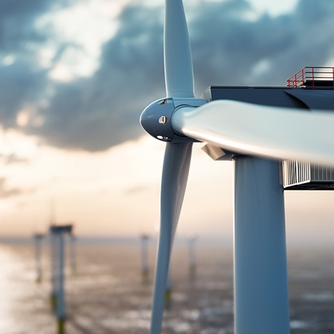 Close-up of a wind turbine by the coast, with several turbines in the background under a dramatic sky.