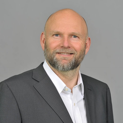 A person in a business suit poses against a plain grey background, showcasing a professional appearance.