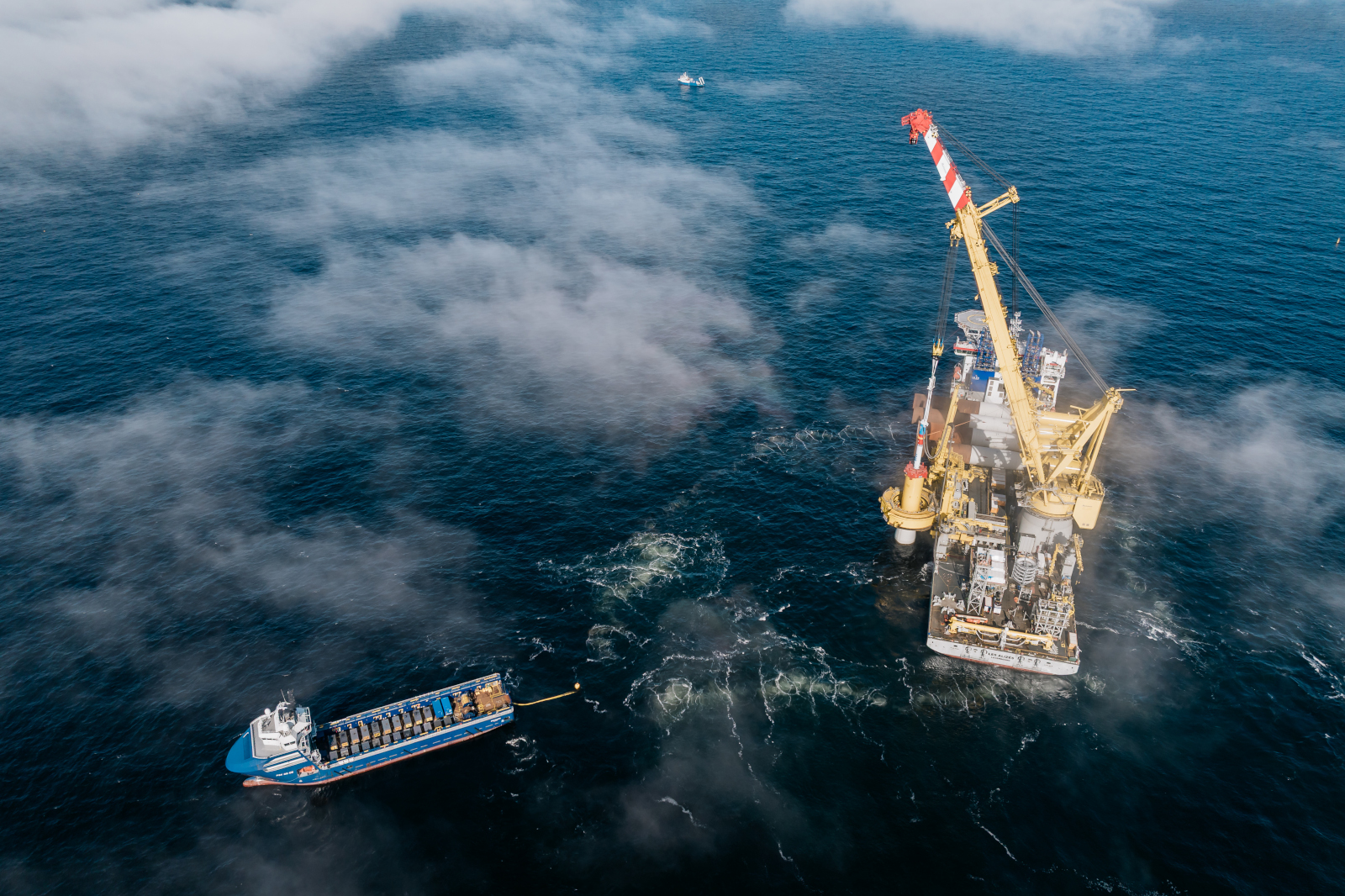 An aerial view of an offshore oil rig with a crane and a supply vessel in foggy waters.