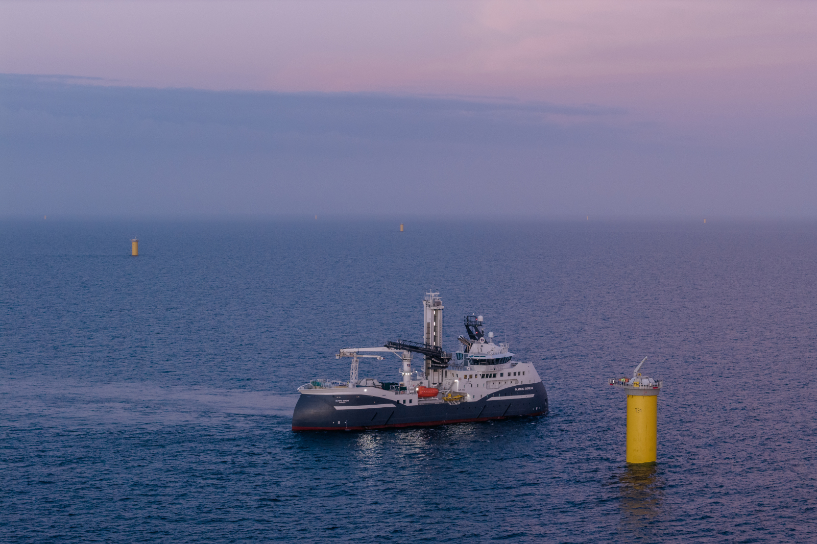 A research vessel manoeuvres in the sea, with yellow pillars rising from the water in the background during twilight.