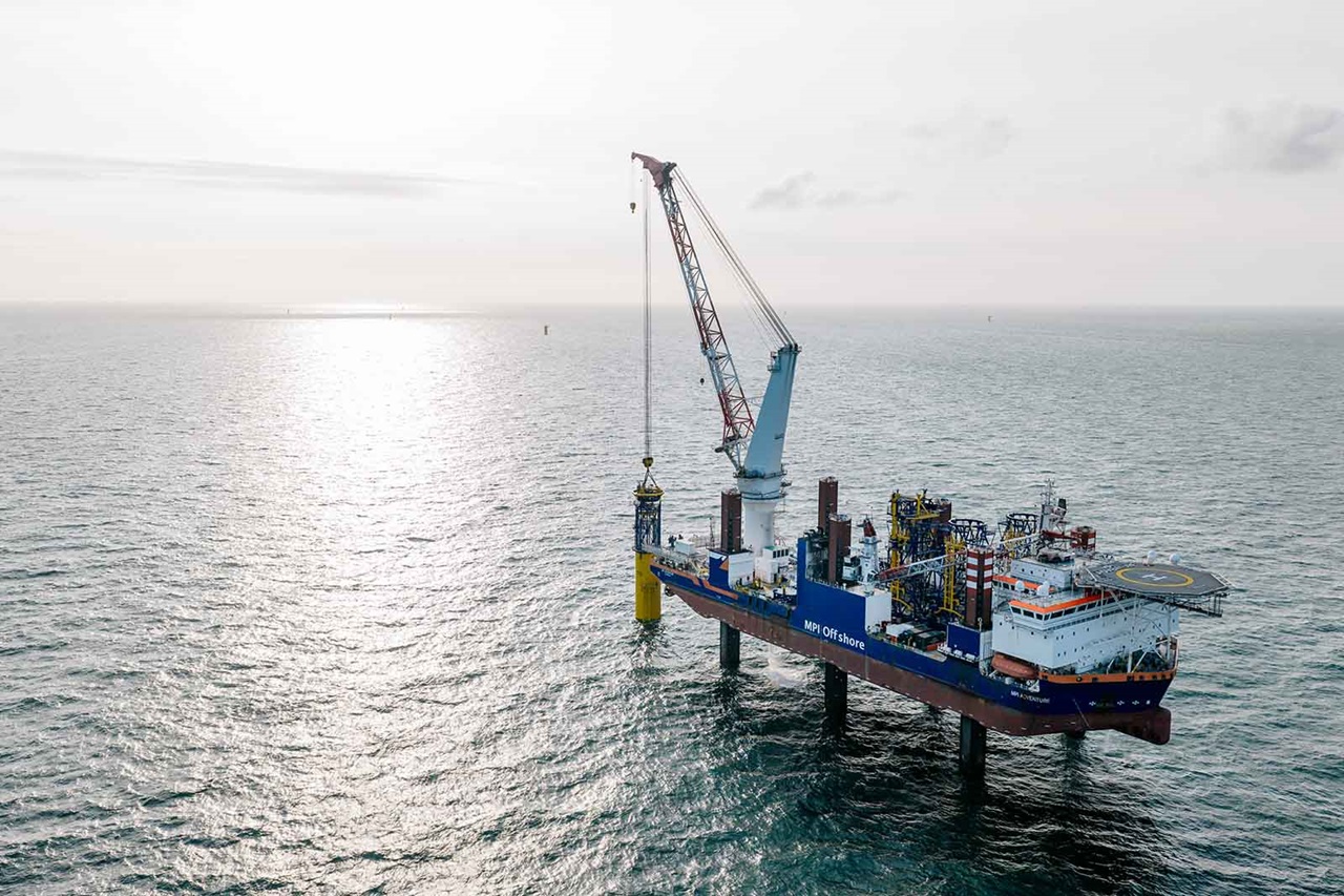 A ship with a large crane is lifting a cylinder from the sea surface under a bright sky.