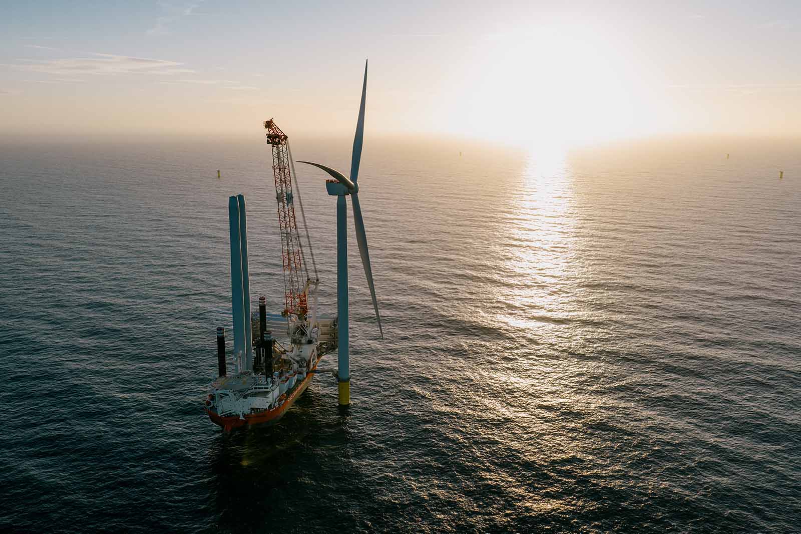 Offshore wind turbine with service vessel and crane at sunset