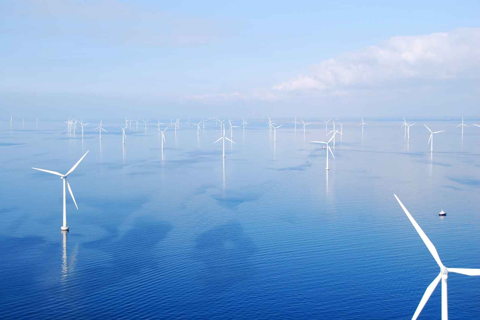 A wind turbine in the sea with multiple wind turbines in the background and calm water.